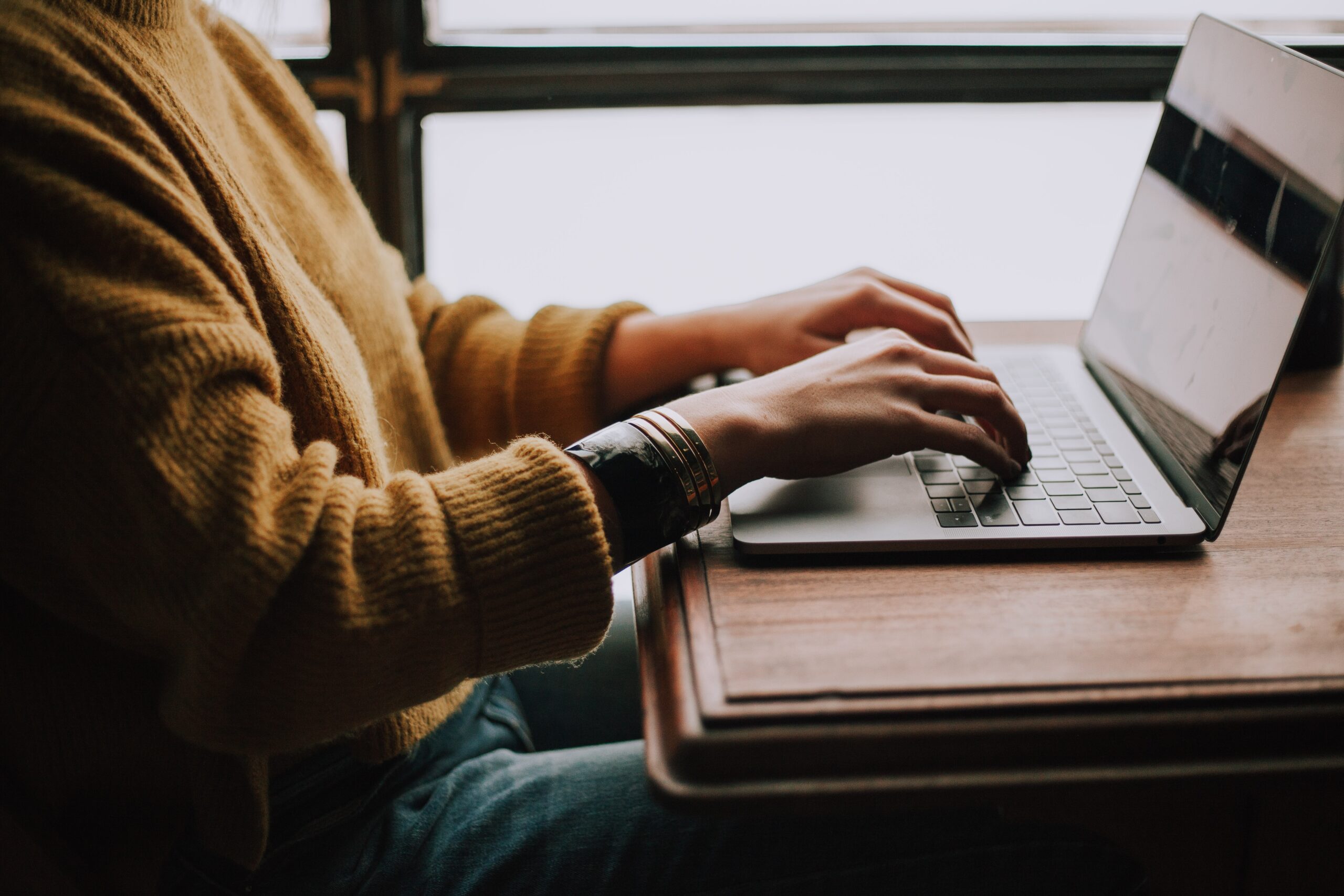 Image of women typing on a computer in a yellow sweater.