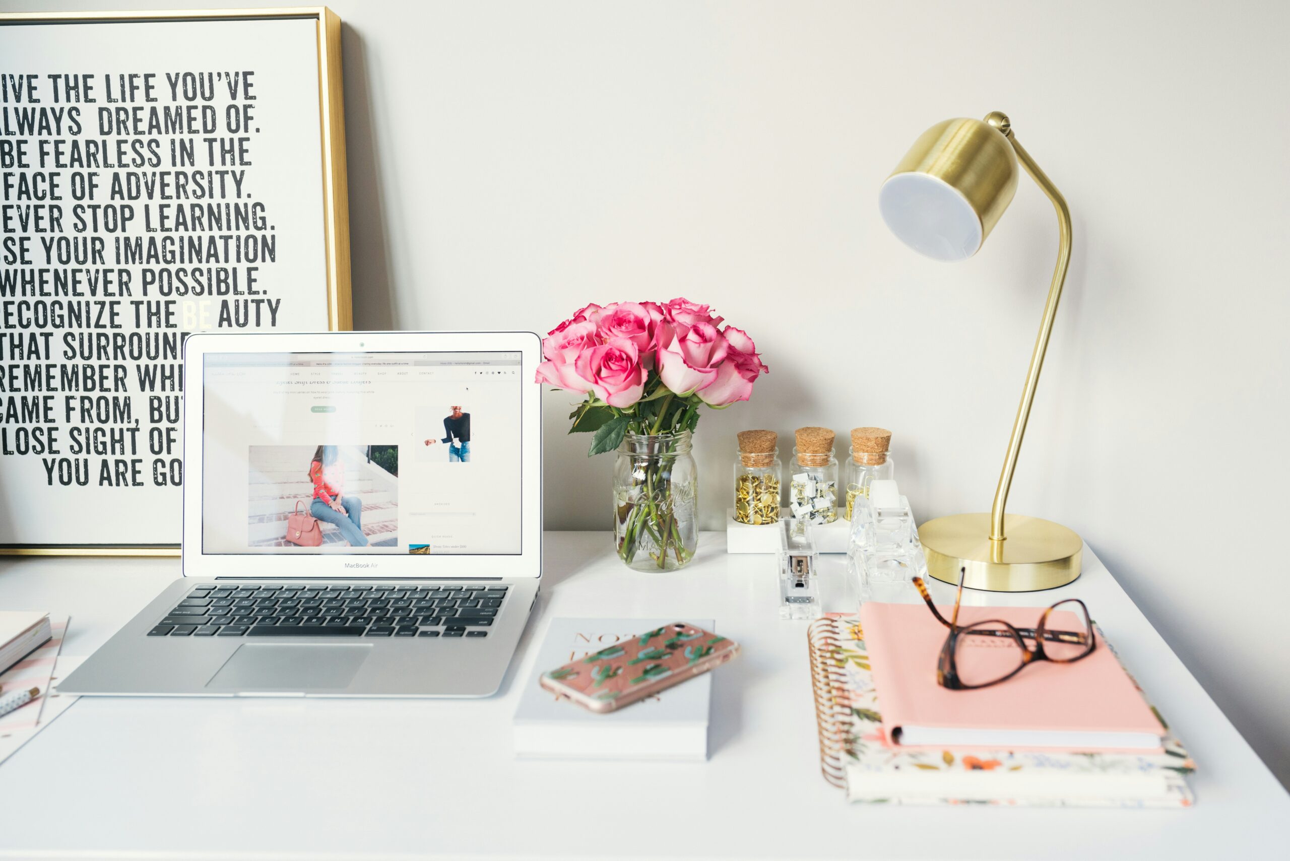 Image of a computer at a desk with a lamp, book, and flowers